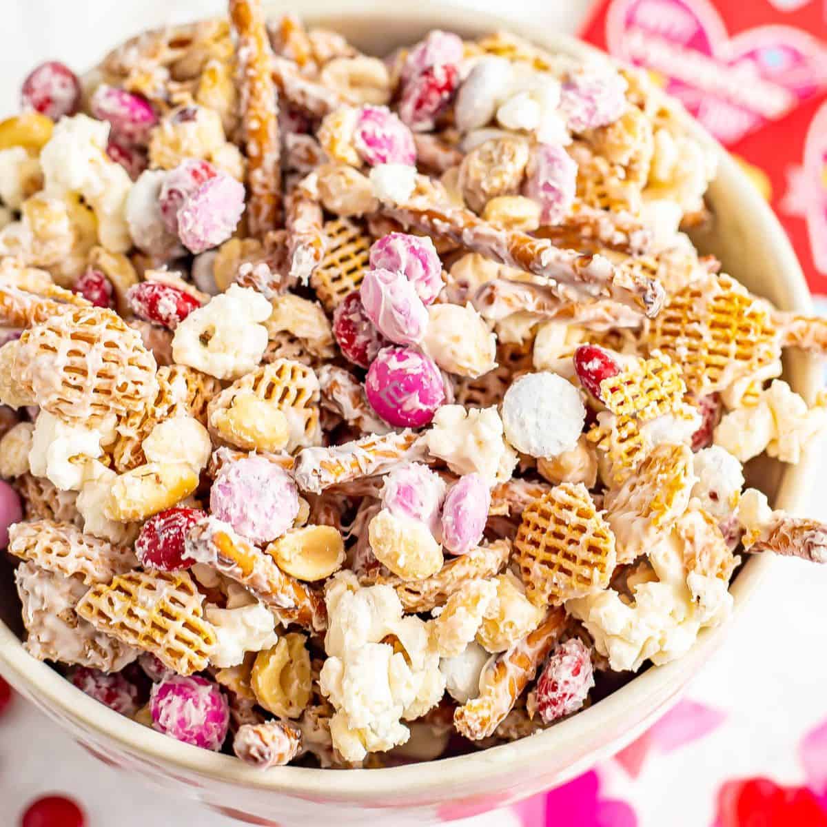 A white chocolate covered Valentine's Day snack mix with pretzels, cereal, peanuts and M&Ms.
