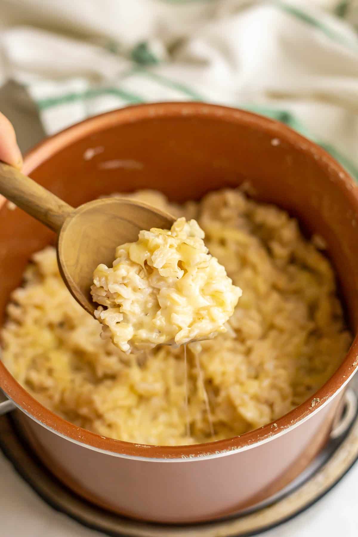 A scoop of cheesy rice being lifted out of a copper pan.