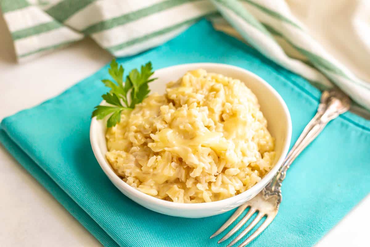 Brown rice with cheese in a small white serving bowl and a fork to the side.