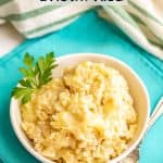 A bowl of cheesy brown rice with a garnish of parsley on the side and a fork nearby on a teal napkin and a text overlay on the photo.