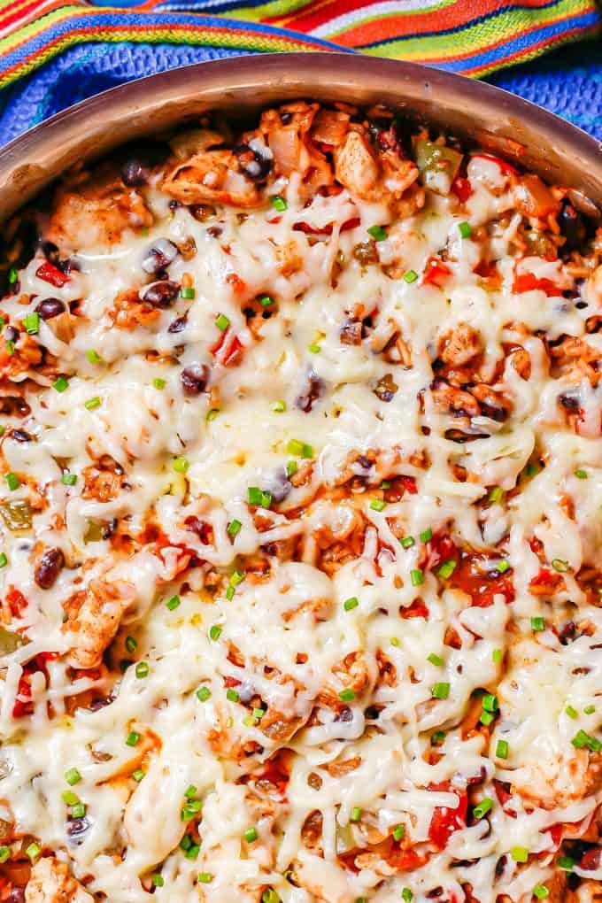 Close up of cheesy chicken fiesta in a large deep skillet with rice, beans, tomatoes and peppers.