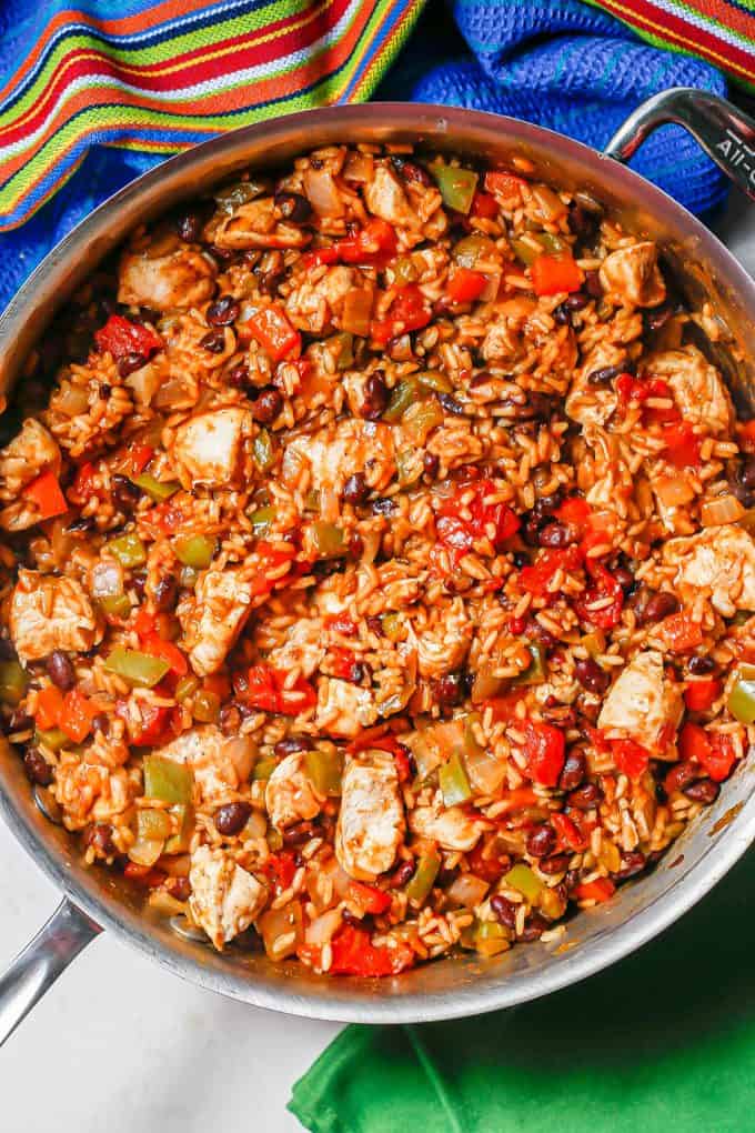 A mixture of cubed chicken, cooked rice with black beans, tomatoes, peppers and onions in a large deep skillet.