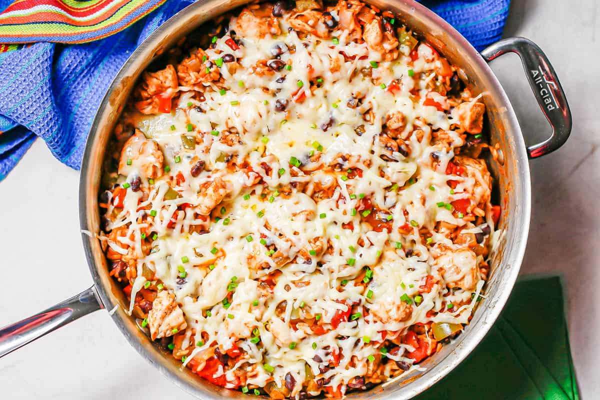 A cheesy chicken and rice skillet with black beans, tomatoes and peppers.