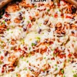 Close up of cheesy chicken fiesta in a large deep skillet with rice, beans, tomatoes and peppers with a text overlay on the photo.