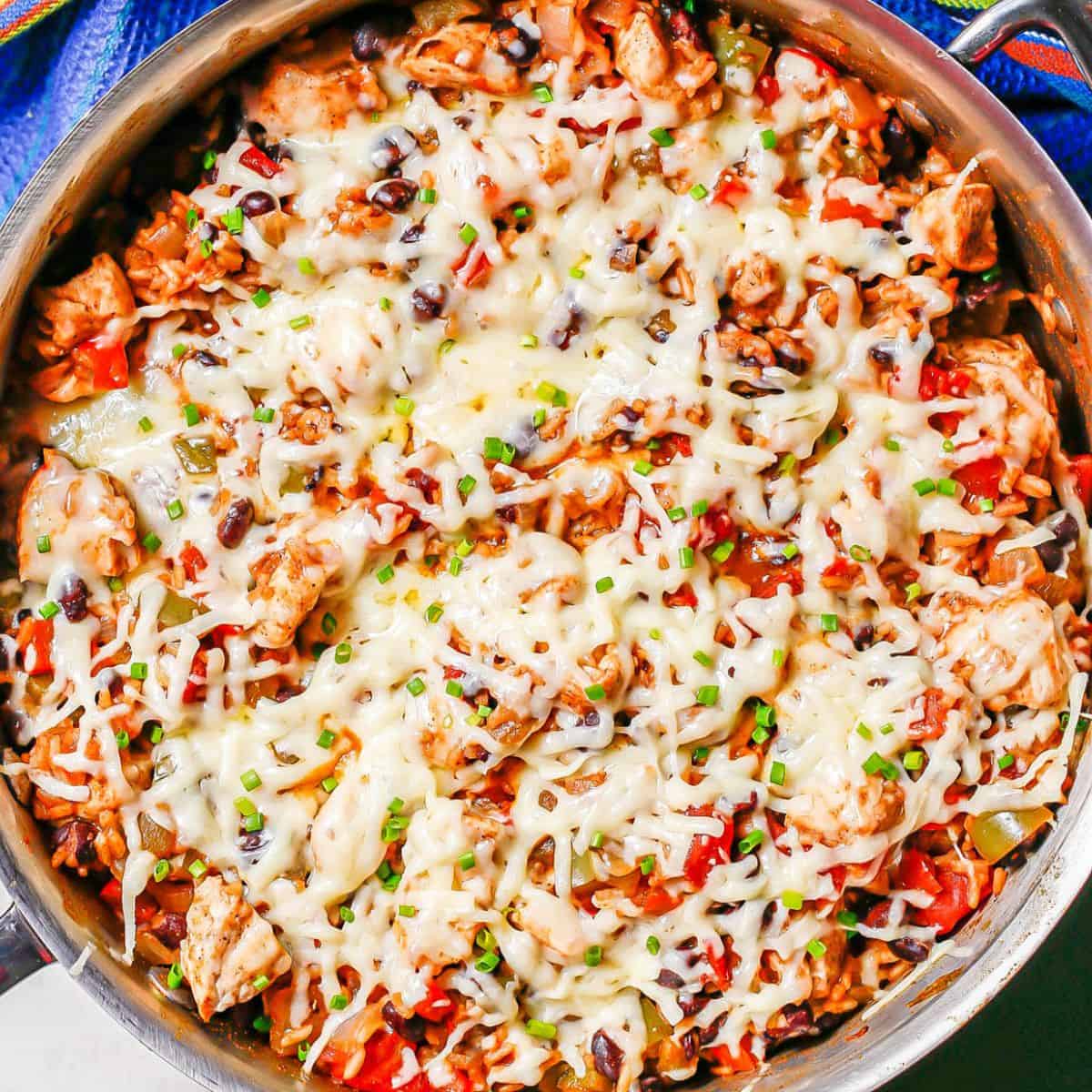 Close up of a cheesy chicken and rice skillet in a large all clad pan.