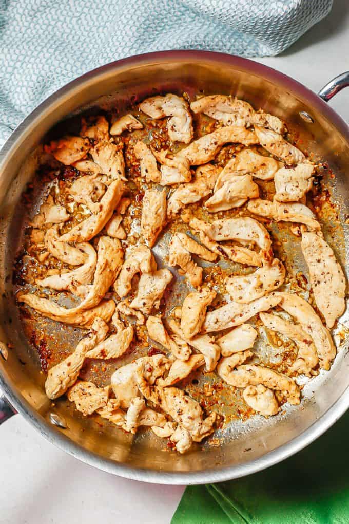 A skillet with seared chicken strips and garlic.