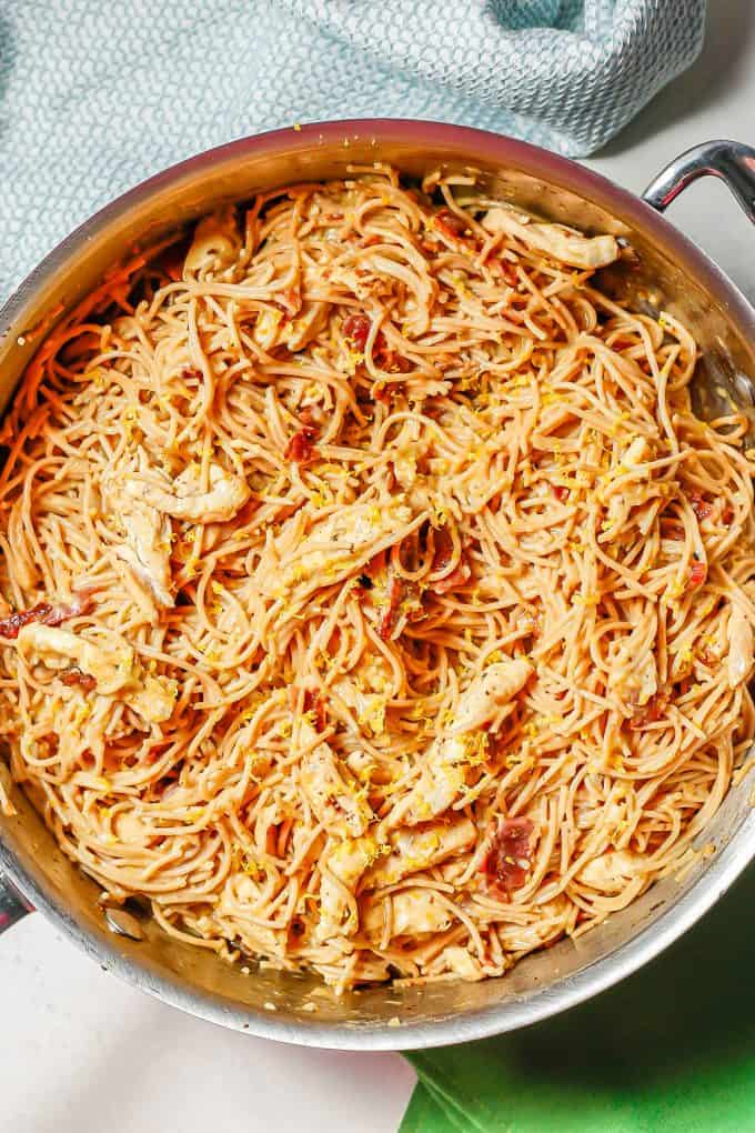 A large deep skillet with spaghetti, chicken strips, bacon topped with lemon zest.