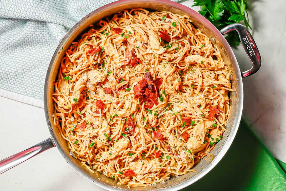 Chicken carbonara in a large deep skillet topped with extra bacon and chopped fresh parsley with parsley sprigs to the side.
