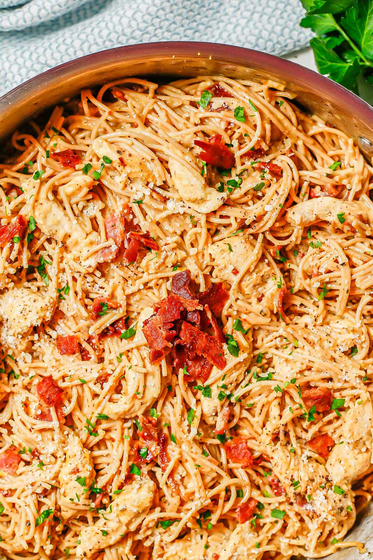 Close up of chicken carbonara in a large deep skillet topped with extra bacon and chopped fresh parsley.