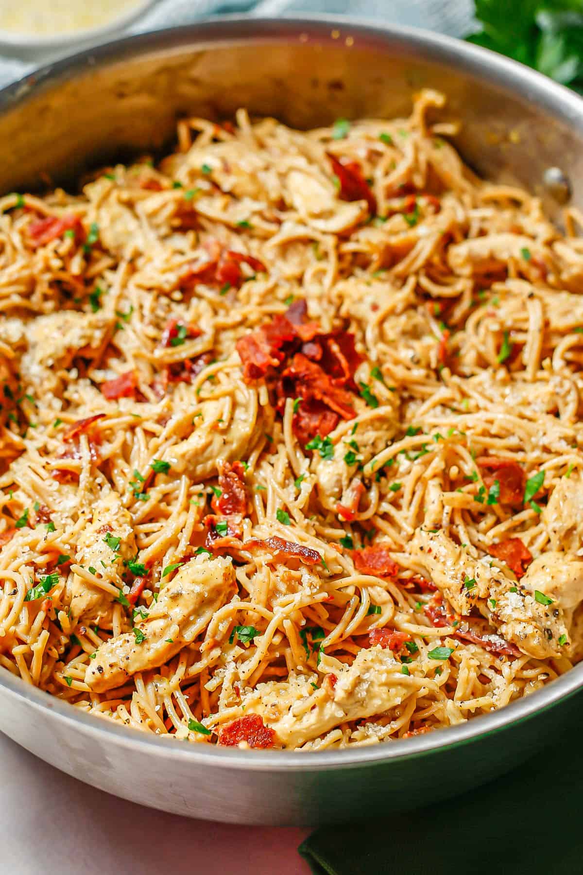 Side view of homemade chicken carbonara in a large deep skillet topped with extra bacon and chopped fresh parsley.