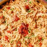 Close up of chicken carbonara in a large deep skillet topped with extra bacon and chopped fresh parsley and a text overlay on the photo.