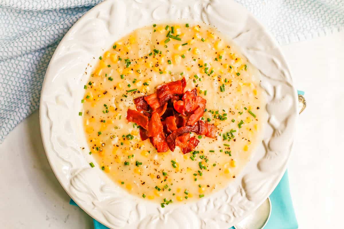 Corn chowder topped with chives and bacon in a white soup bowl.