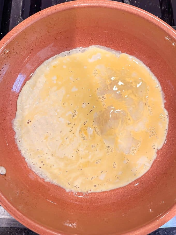 A thin layer of egg cooking in a medium copper skillet.