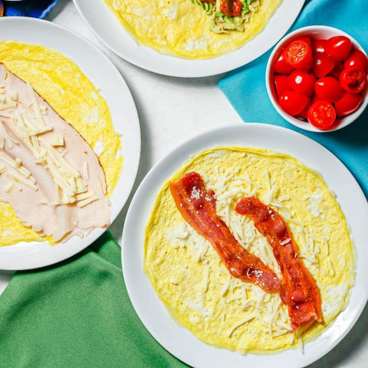 Two egg wraps on round white plates with different toppings set on colorful napkins.