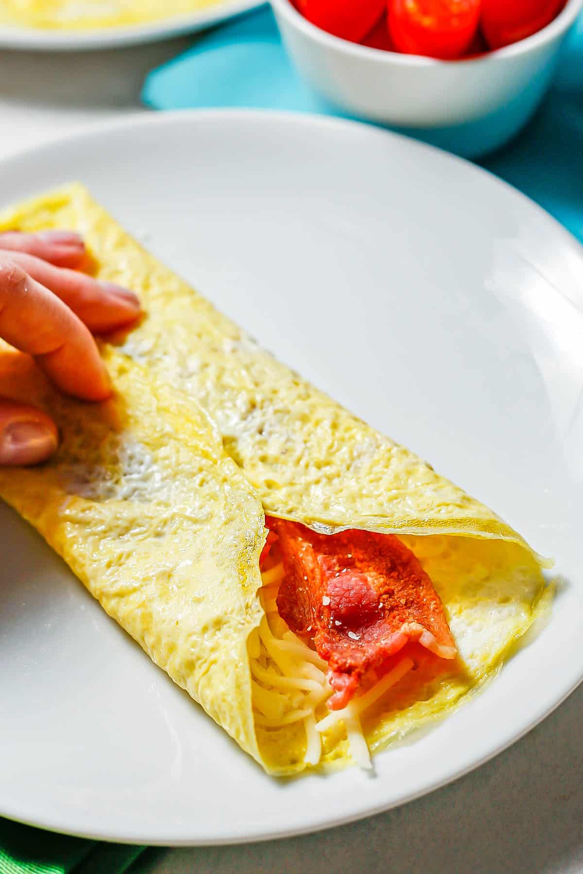 A hand holding a folded over egg wrap with cheese and bacon on the inside.