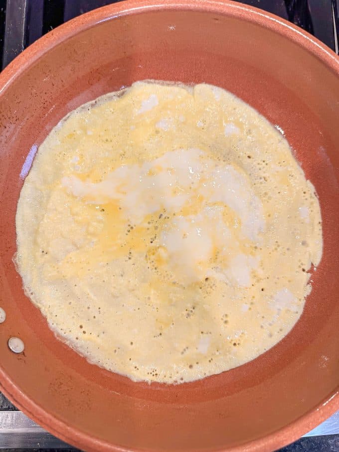 A thin layer of egg almost finished cooking in a medium copper skillet.