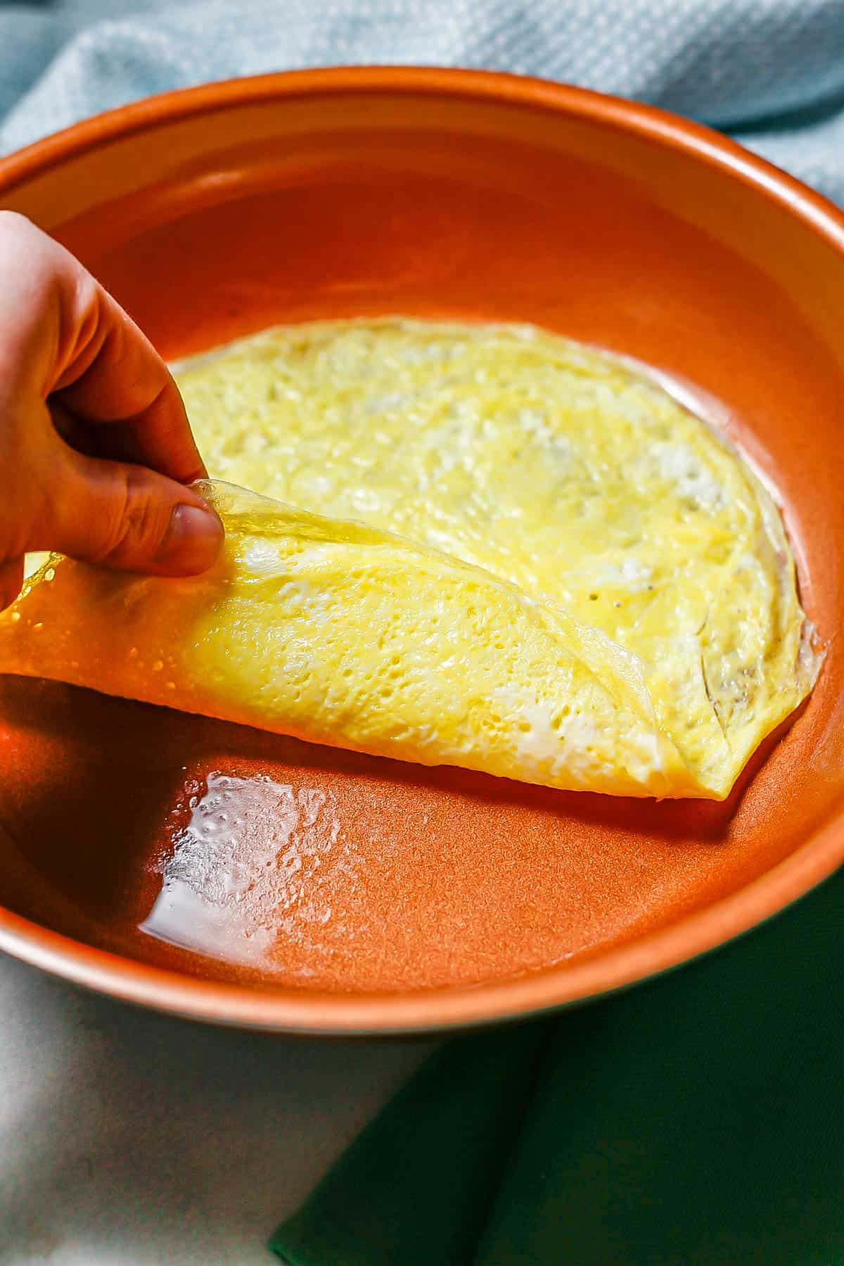 A hand lifting up a thin egg wrap in a copper skillet after it's cooked.