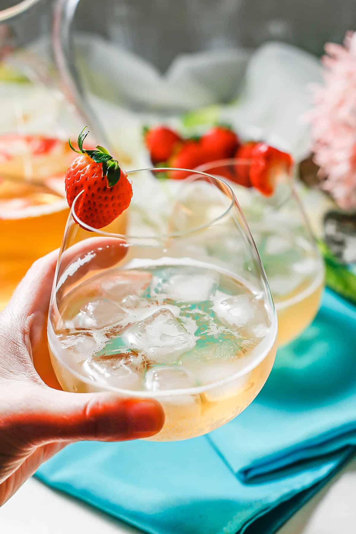 A hand holding up a stemless wine glass filled with an elderflower champagne cocktail garnished with a strawberry.