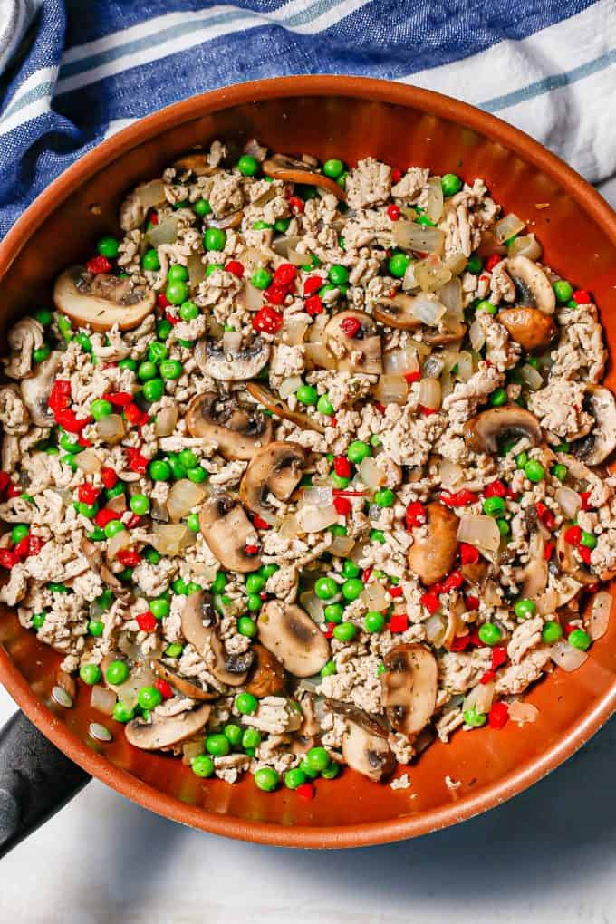Cooked ground chicken and mushrooms with peas and pimientos in a large copper skillet.