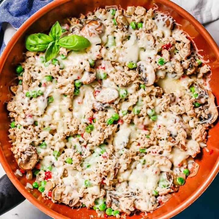 Ground chicken mixed with mushrooms, onions, peas and pimientos in a large copper skillet topped with melted mozzarella cheese.