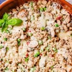 Close up of a cheesy ground chicken and mushroom skillet with peas and pimientos and a sprig of basil to the side and a text overlay on the photo.