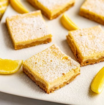 Close up of a lemon bar topped with powdered sugar on a serving plate.