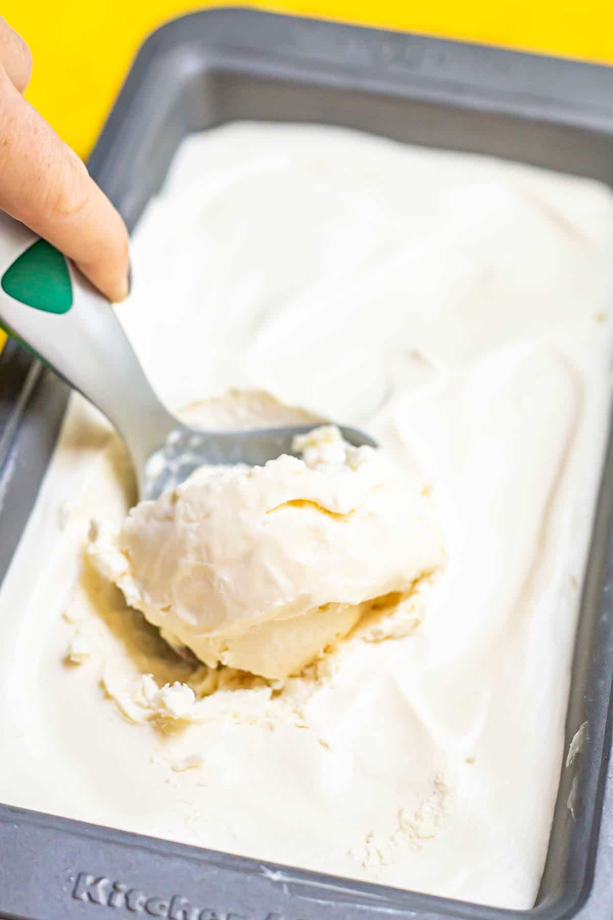 A scoop of homemade vanilla ice cream being scraped up from a silver pan.