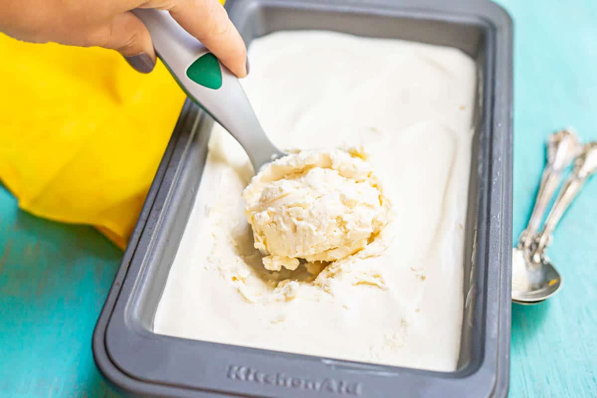 An ice cream scoop taking a scoop of vanilla ice cream from a silver pan.