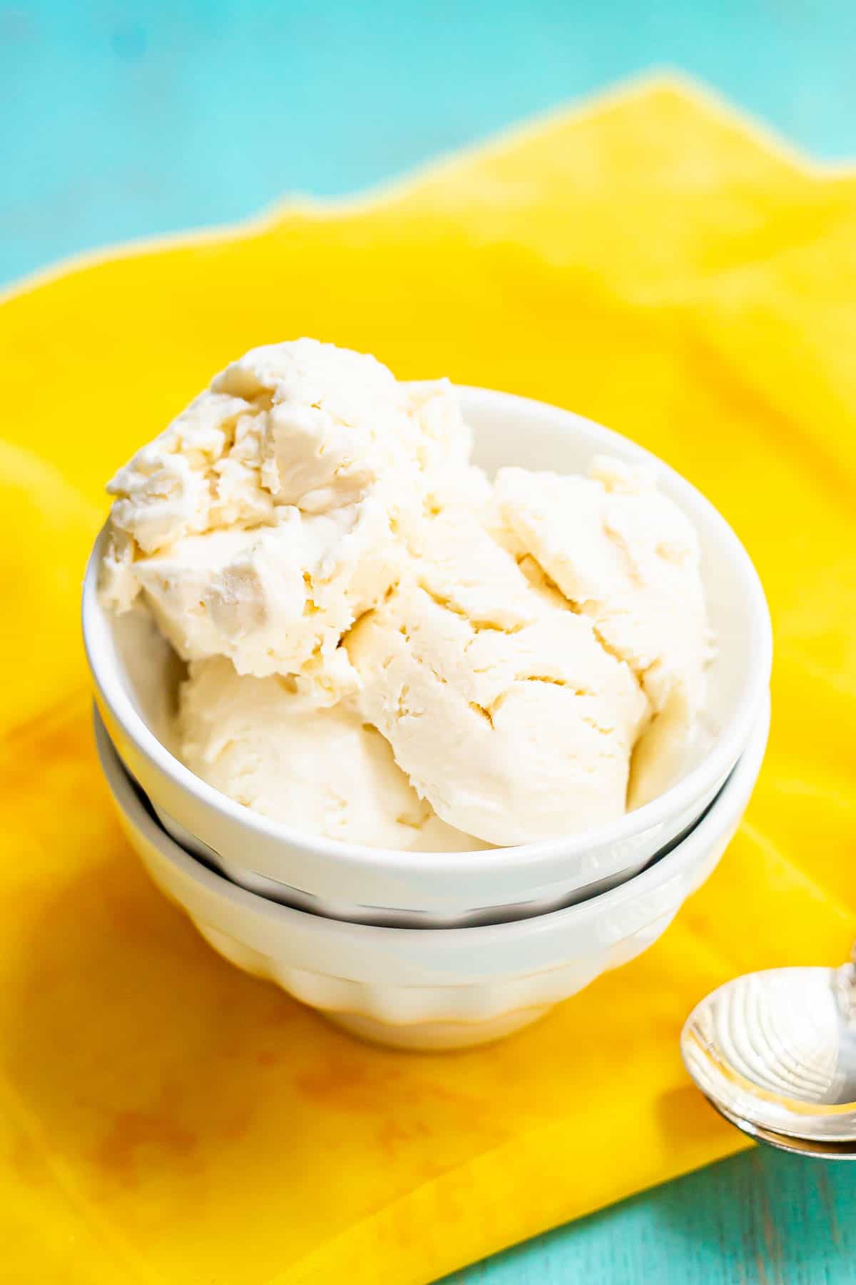Vanilla ice cream served in a stacked white bowl on a yellow fabric with spoons nearby.