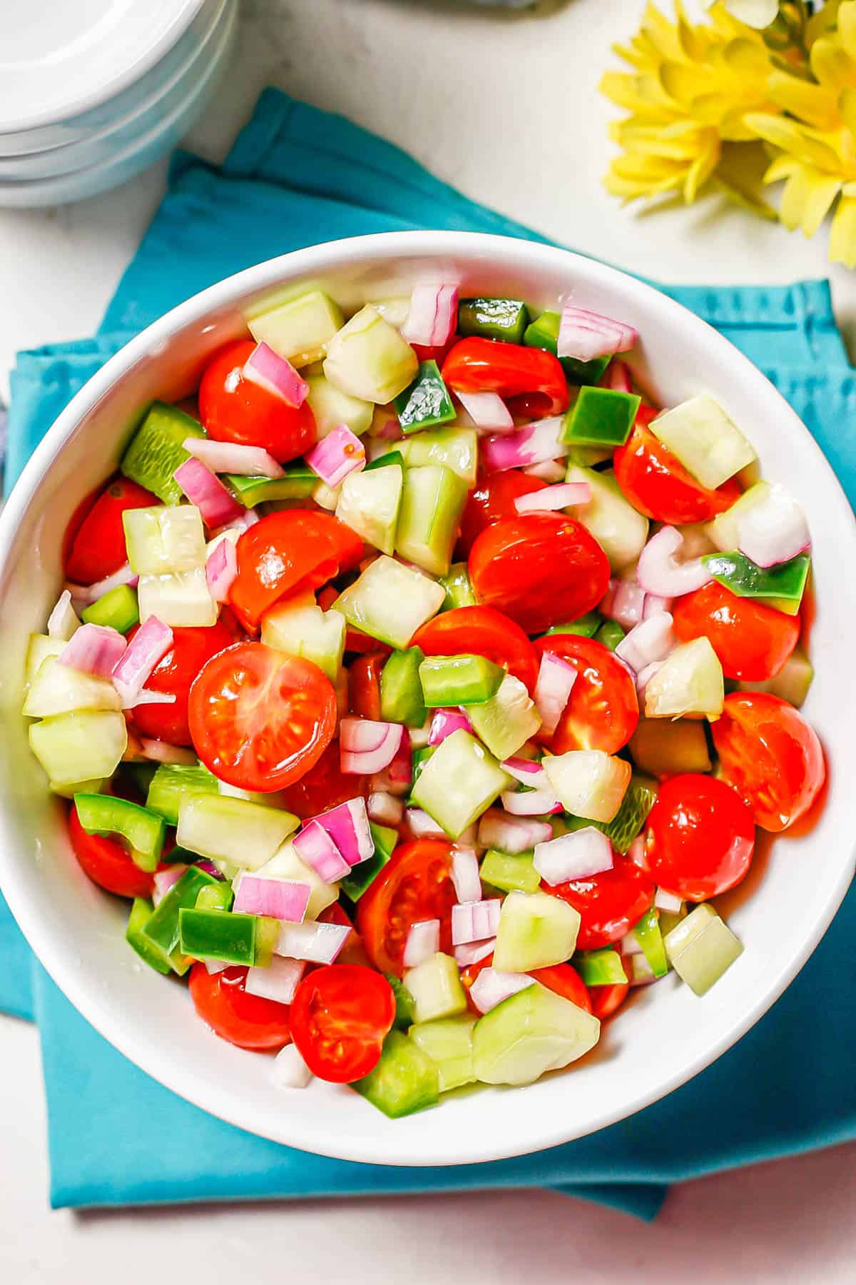 A colorful marinated veggie salad with tomatoes, cucumber, green pepper and red onion in a large white serving bowl.