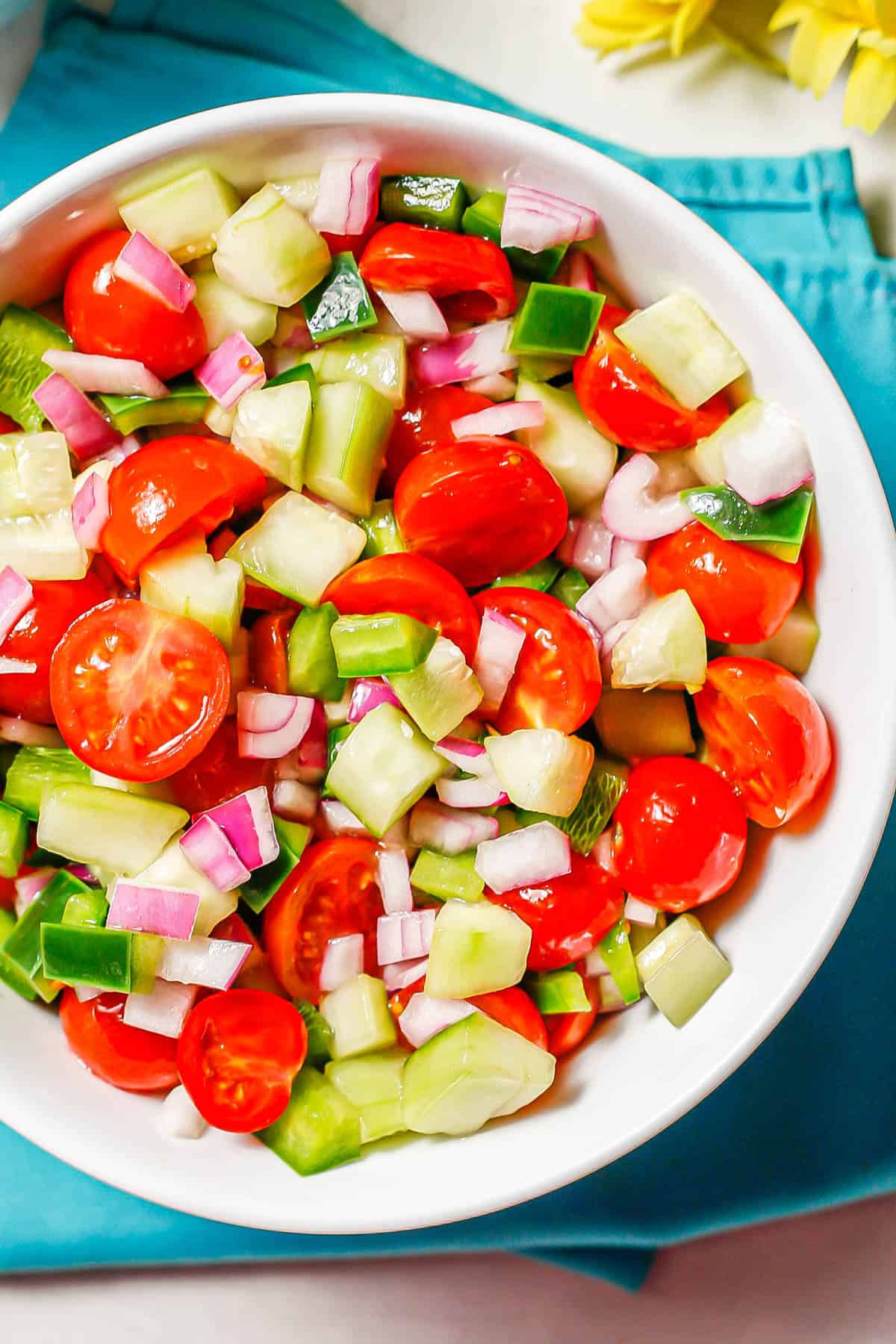 Close up of a colorful marinated vegetable salad in a large white serving bowl set on teal napkins.