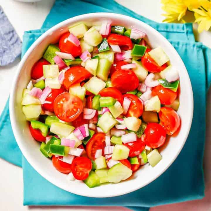 Marinated vegetables in a white serving bowl set on teal napkins with some yellow flowers to the side.