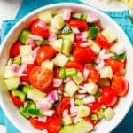 A colorful marinated veggie salad with tomatoes, cucumber, green pepper and red onion in a large white serving bowl with a text overlay on the photo.