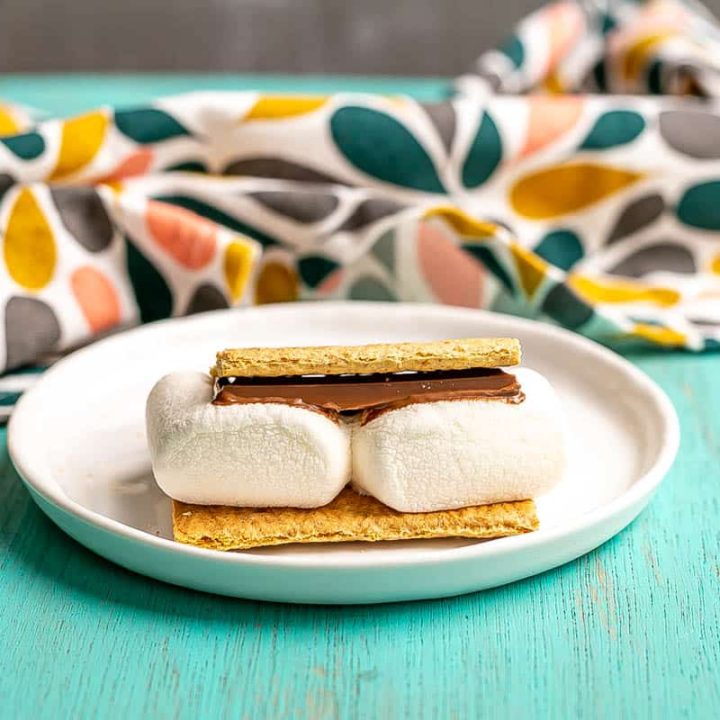 A single s'mores on a small white plate after being cooked in the microwave.