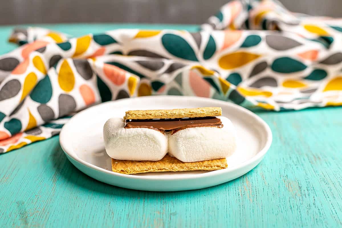 A single s'mores on a small white plate after being cooked in the microwave.