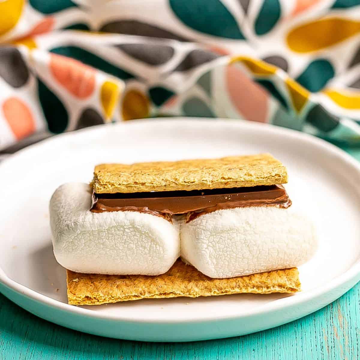 Close up of s'mores on a small white plate with a colorful napkin in the background.