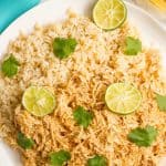 A serving plate loaded with steamed brown rice and shredded tequila chicken topped with cilantro and lime slices.