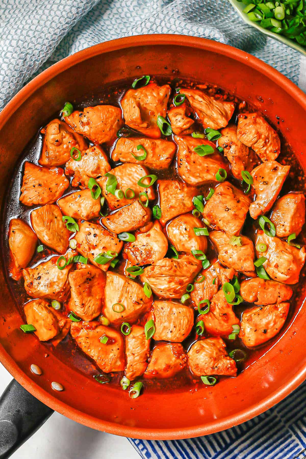 Bourbon chicken in a large copper skillet with sliced green onions on top.