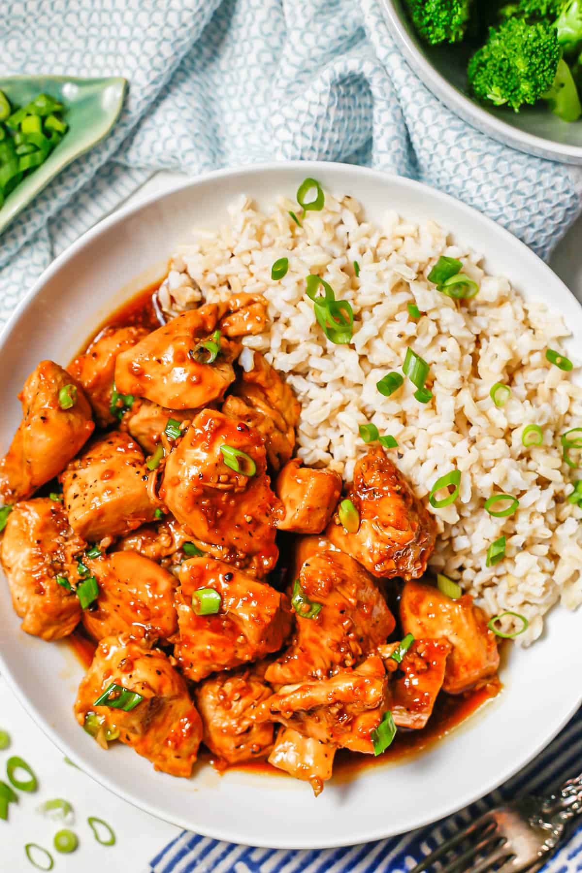 Bourbon chicken served with rice and sliced green onions in a low white bowl.