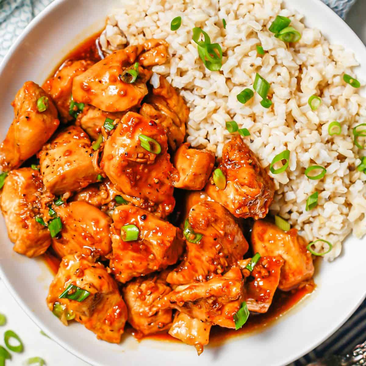 Close up of bourbon chicken and rice in a low white bowl.