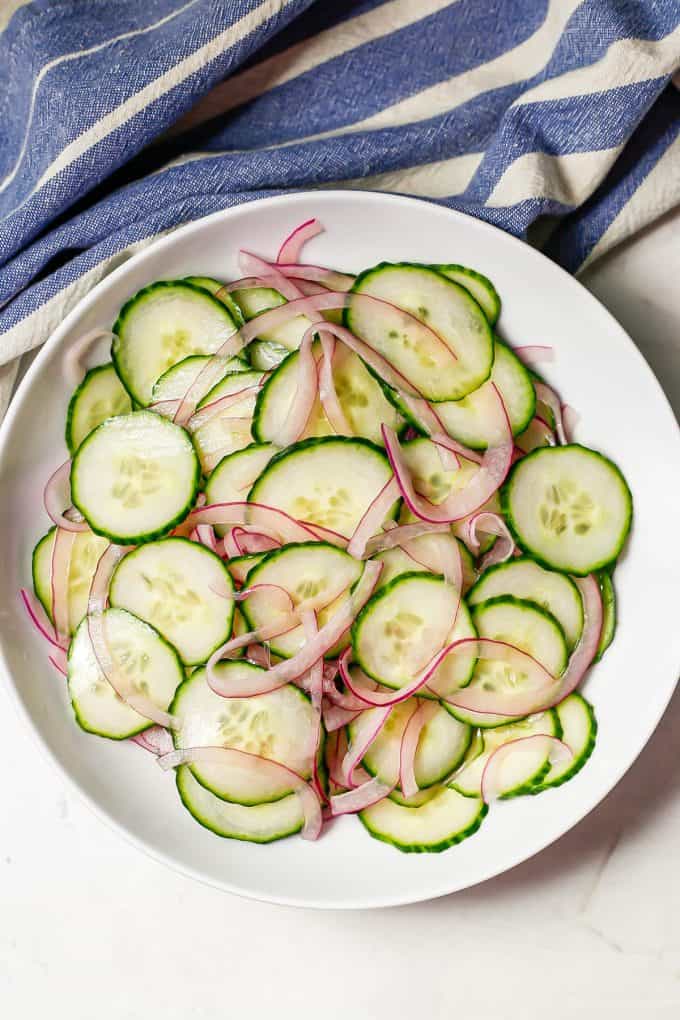 Thinly sliced cucumber and red onion slices marinated in a low white bowl.