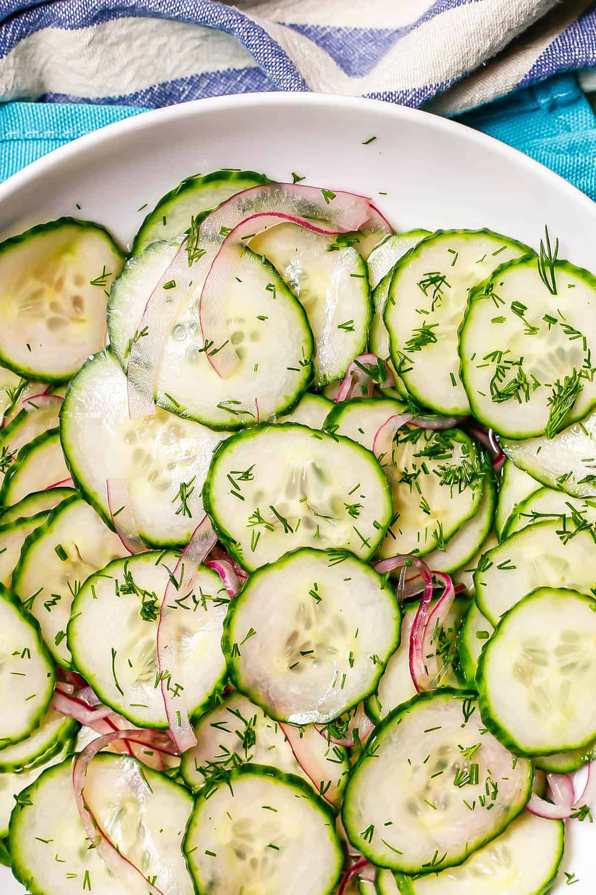 Close up of a marinated cucumber salad in a low white bowl with fresh dill on top.