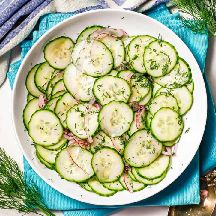 A cucumber salad served in a low white bowl with sprigs of fresh dill to the side.