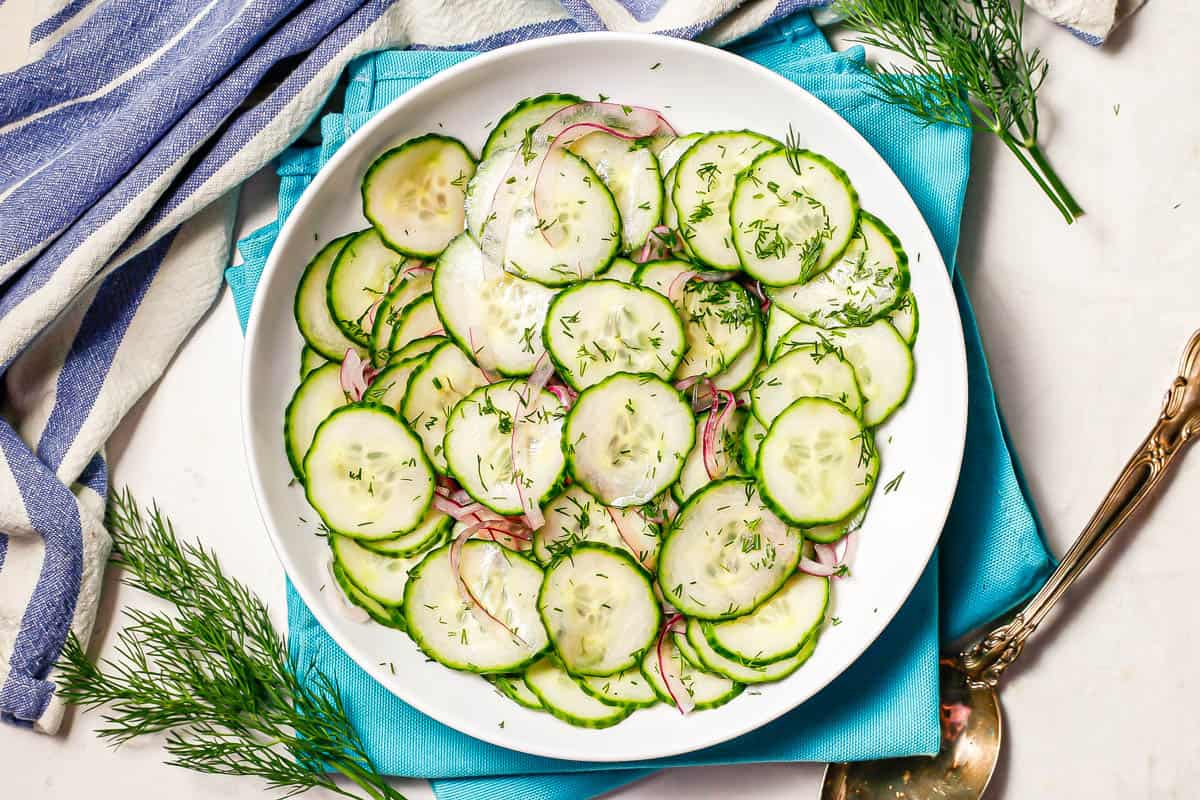 A cucumber salad served in a low white bowl with sprigs of fresh dill to the side.