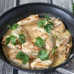 Chunks of chicken breasts cooked in a pan with a creamy sauce and topped with fresh parsley.