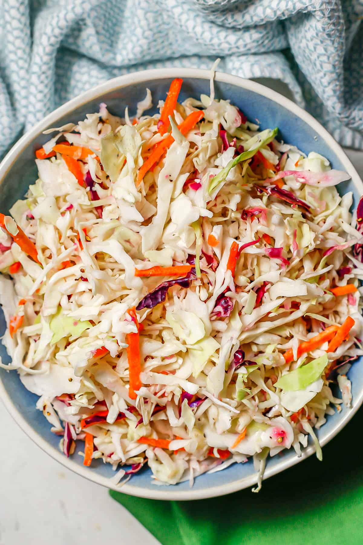 No mayo coleslaw in a blue and white bowl with colorful napkins nearby.