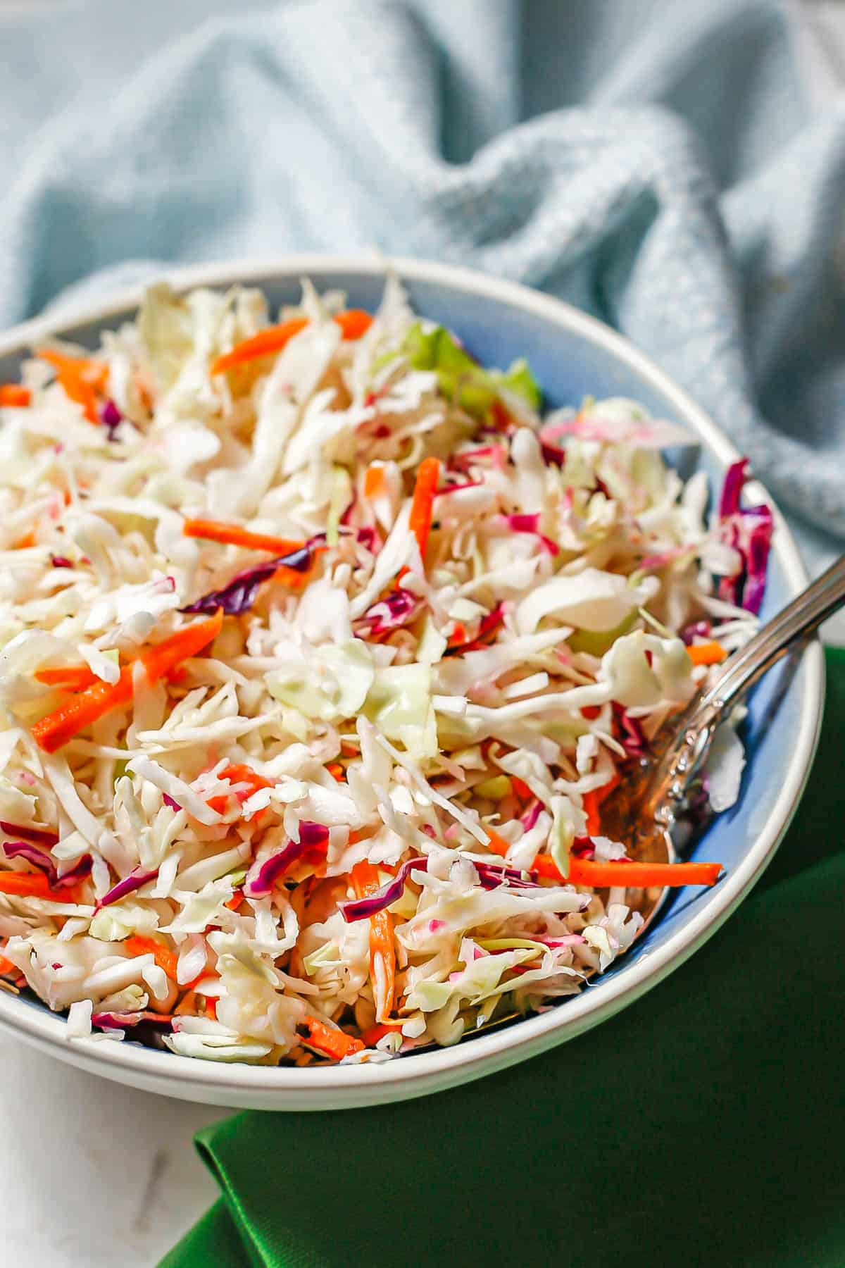 A blue and white bowl with a vinegary coleslaw mix and a fork resting in the side.