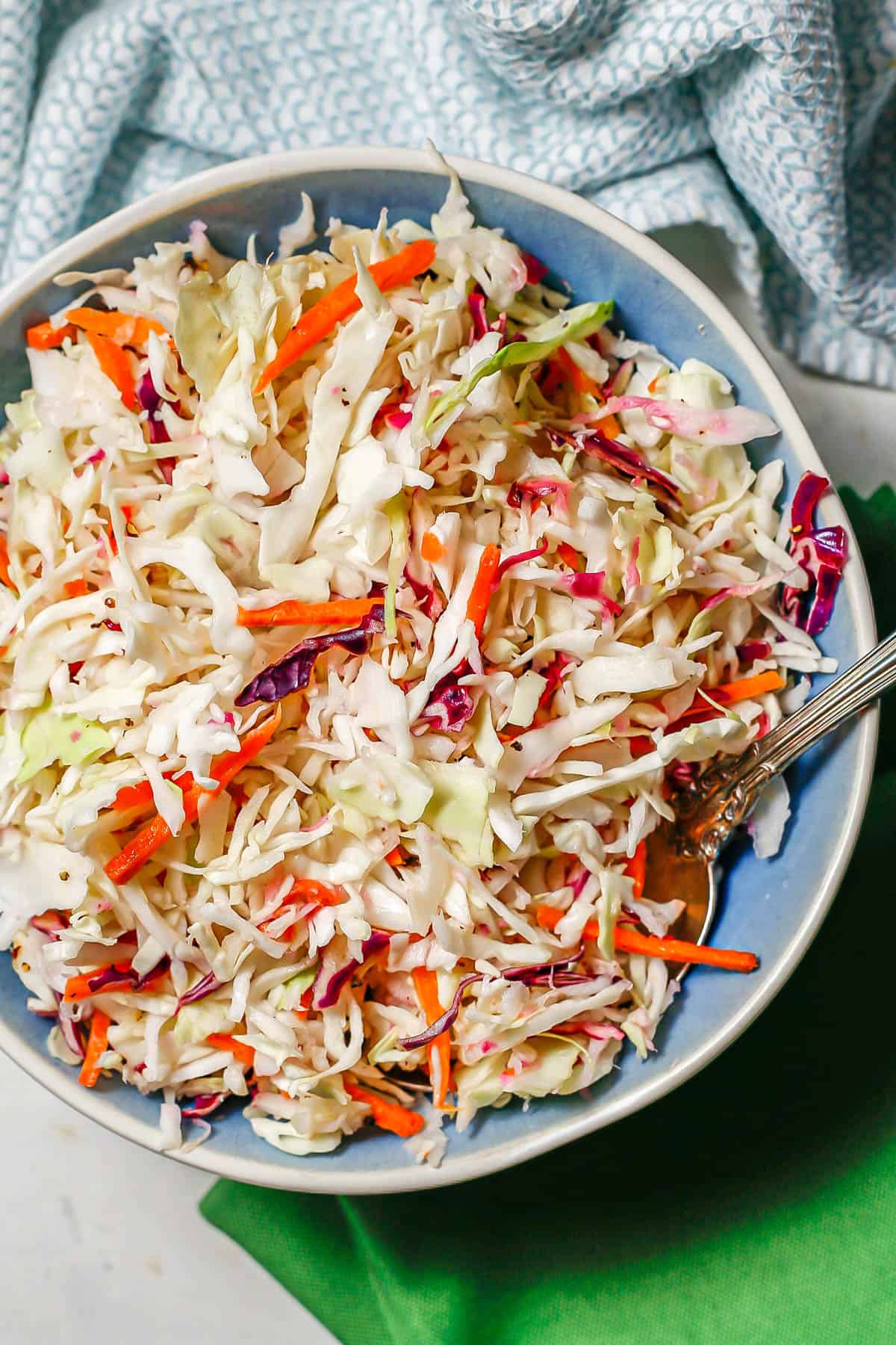A blue and white bowl with a coleslaw mix and a fork resting in the side.