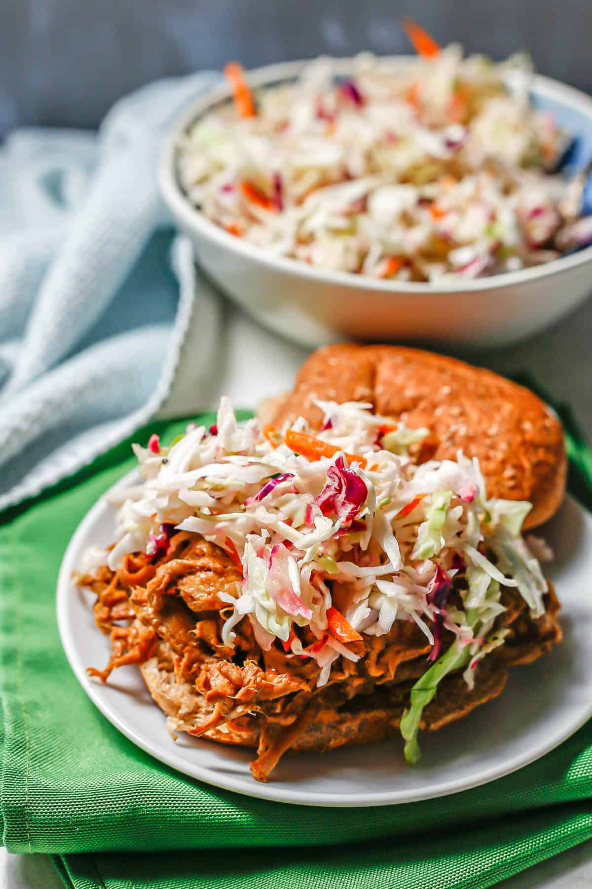 A pulled pork sandwich with coleslaw on top on a small white plate.