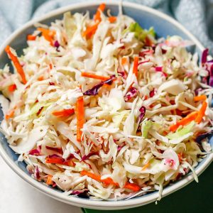 Close up of no mayo coleslaw in a blue and white bowl with colorful napkins nearby.